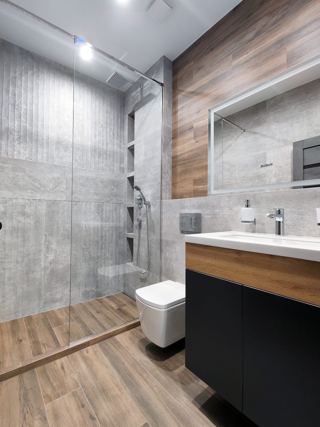 Nowoczesna łazienka z kabiną prysznicową typu walk-in, drewnopodobnymi płytkami na podłodze i ścianie, oraz szafką umywalkową w kolorze czarnym i drewnianym blatem.