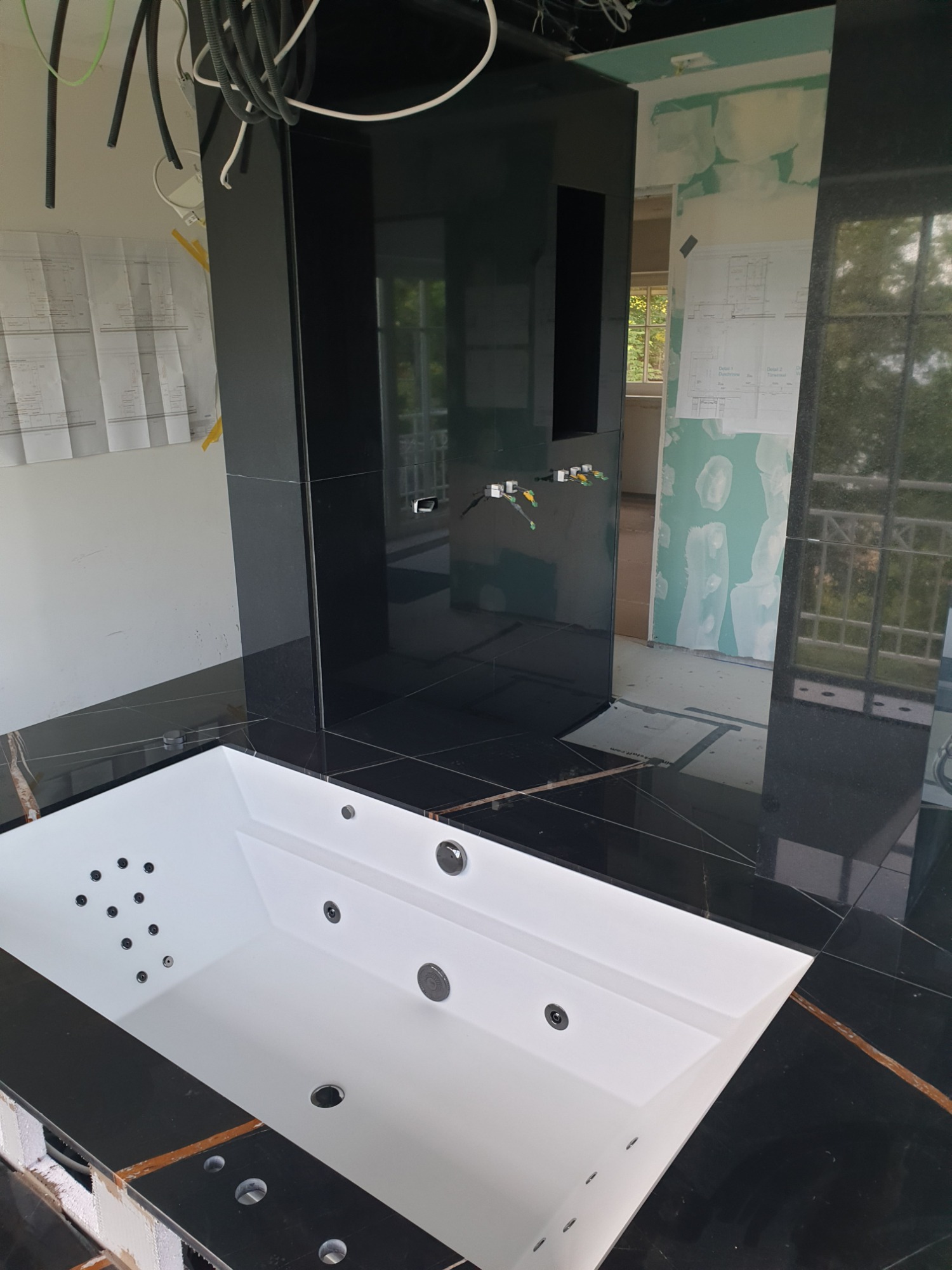 Montaż wanny z hydromasażem na tle czarnej, marmurowej posadzki i ściany, widoczne niedokończone prace wykończeniowe i wystające kable.
