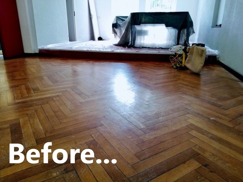 Stary parkiet ułożony w jodełkę, widoczne ślady użytkowania i zarysowania, przygotowany do renowacji, z tekstem 'Before...' nałożonym na dolną część zdjęcia.