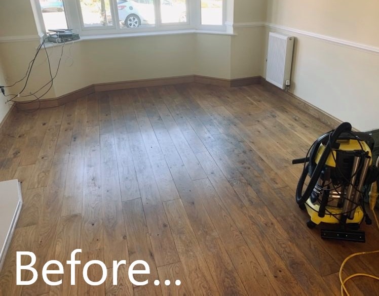 Pokój przed renowacją: widoczna drewniana podłoga z wyraźnymi śladami użytkowania, żółty odkurzacz przemysłowy stoi w rogu, tekst 'Before...' nałożony na dolną część zdjęcia.
