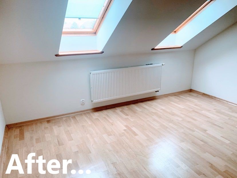 Jasne panele podłogowe ułożone w skos w pokoju na poddaszu z oknami dachowymi i białymi ścianami, widoczny grzejnik.