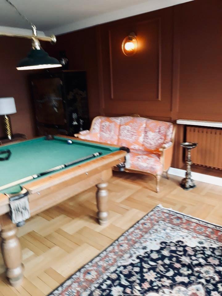 Pokój z brązowymi ścianami, drewnianą podłogą, bilardem, wzorzystą sofą i dywanem w stylu vintage.