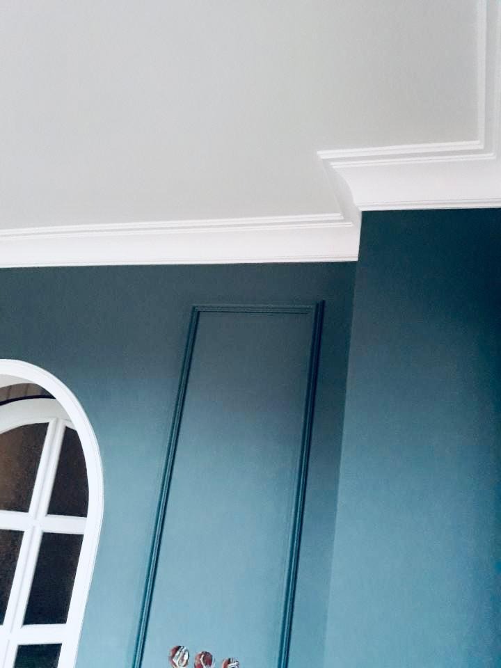 Ściana w odcieniach błękitu i szarości z dekoracyjną sztukaterią, białym oknem łukowym i listwami przypodłogowymi, widok z dołu.