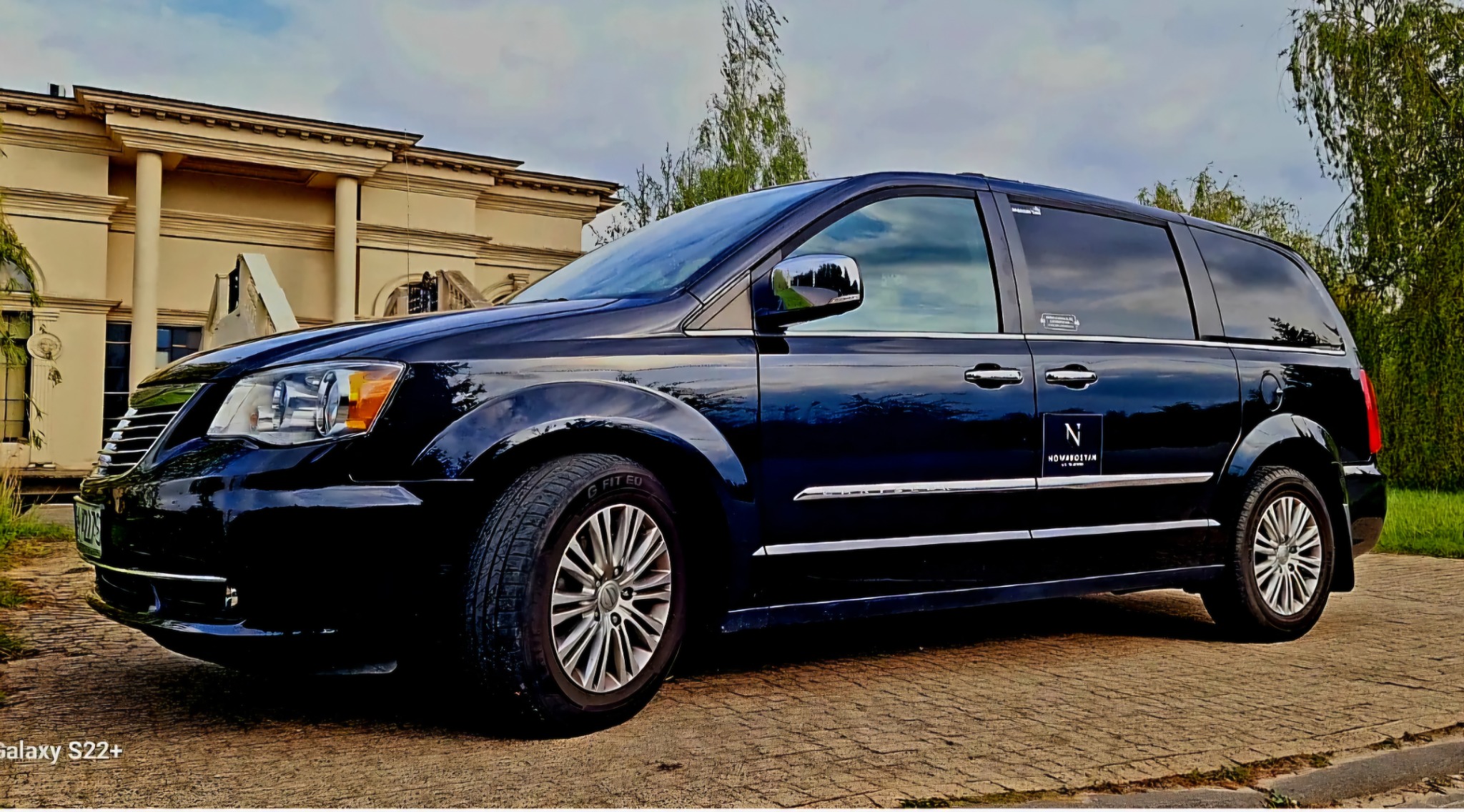 Czarny van z przyciemnianymi szybami i logo firmy transportowej na tle klasycystycznego budynku.