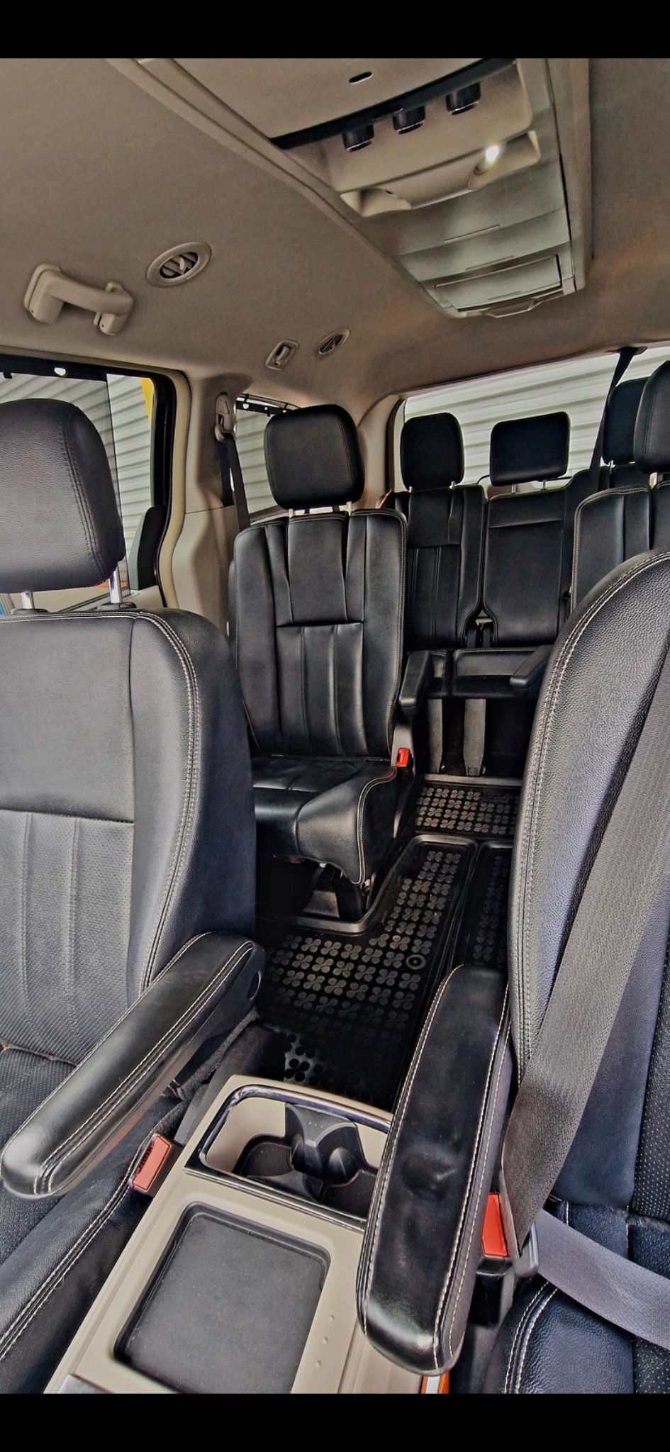 Wnętrze minivana z czarnymi skórzanymi siedzeniami, widok z przodu na drugi i trzeci rząd, gumowe dywaniki z wzorem koniczyny.