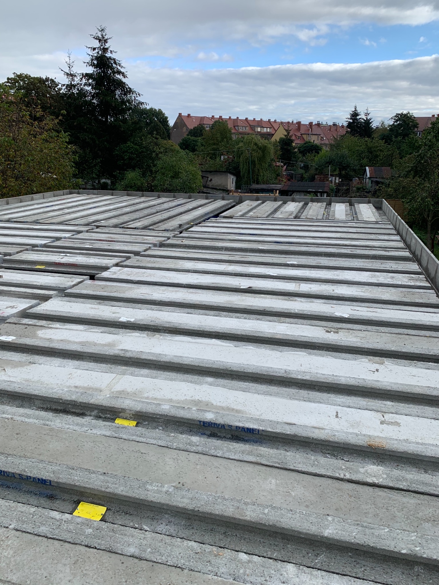 Ułożone płyty stropowe Teriva na budowie, widok z góry, w tle zabudowa jednorodzinna i drzewa.