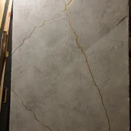 Betonowa ściana z dekoracyjnymi, złotymi pęknięciami w stylu kintsugi, widoczny fragment poziomicy po lewej stronie.