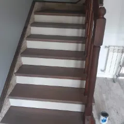 Malowane schody drewniane z białą podstopnicą i ciemnobrązowym stopniem, widoczna puszka farby i zabezpieczająca taśma malarska na dolnym stopniu.