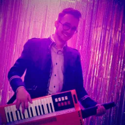 Uśmiechnięty mężczyzna w okularach i marynarce gra na czerwonym keyboardzie na tle błyszczącej, fioletowej kurtyny.