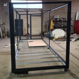 AMJ SPERO SP. Z O.O. - Metalowa konstrukcja szkieletowa w warsztacie, z widocznymi elementami podłogi i ramą, w trakcie montażu. Widoczne narzędzia i materiały w tle.