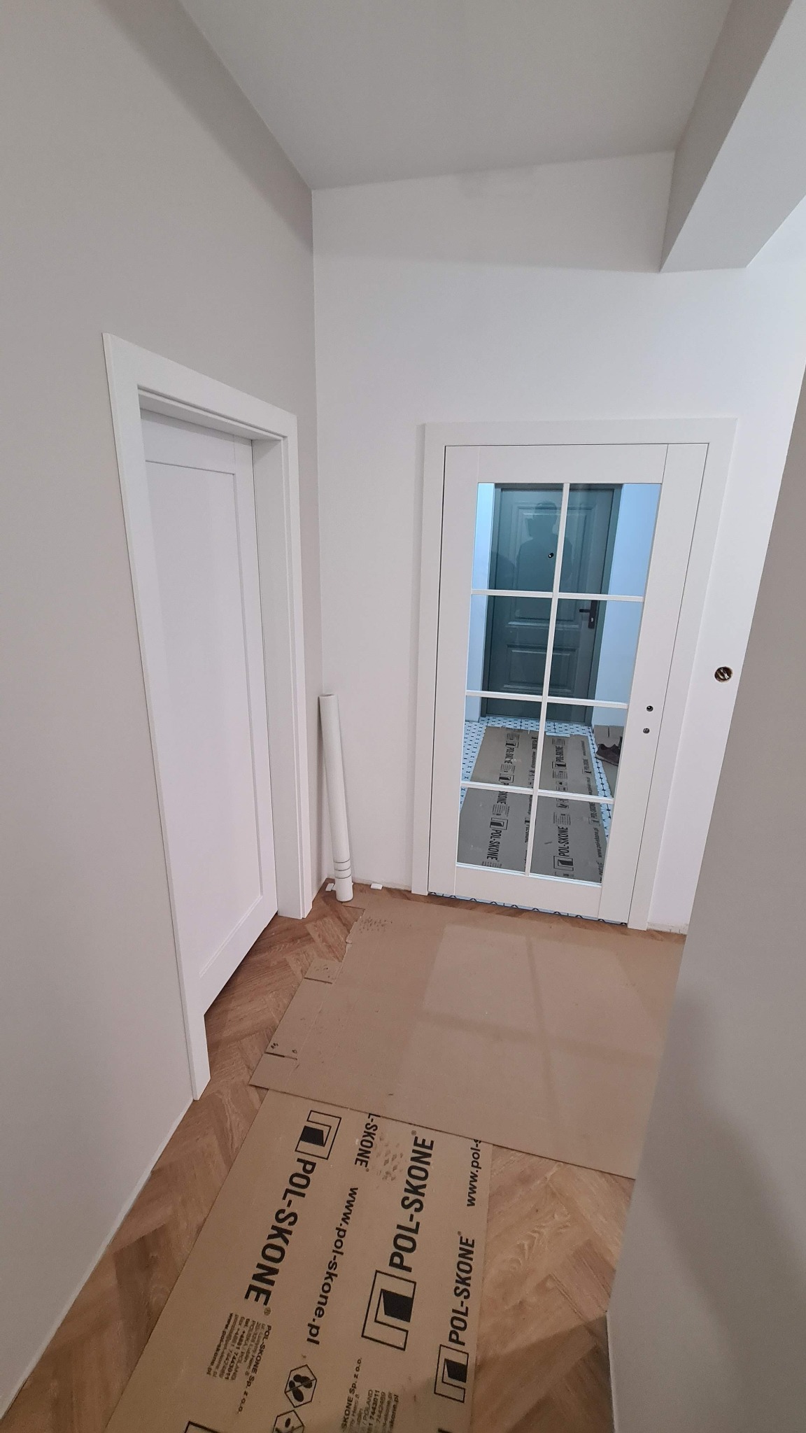 Jasne wnętrze po montażu białych drzwi wewnętrznych z szybami. Podłoga zabezpieczona kartonem. Widoczne dwie pary drzwi.