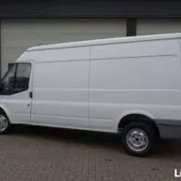 Biały samochód dostawczy Ford Transit na tle szarej, metalowej ściany garażu. Widoczny z boku, lekko od tyłu. Koła lekko zabrudzone.