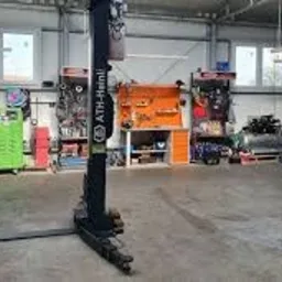 Wnętrze warsztatu samochodowego z podnośnikiem dwukolumnowym ATH-Heinl, stanowiskiem narzędziowym z pomarańczową ścianką perforowaną i licznymi narzędziami oraz sprzętem diagnostycznym w tle.