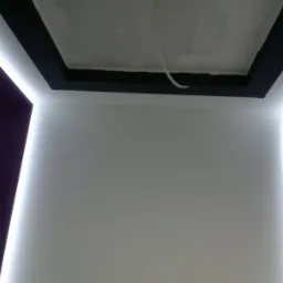 Nowoczesne oświetlenie LED w suficie podwieszanym z czarną ramą i fioletowymi elementami ściennymi, widoczne przewody elektryczne.