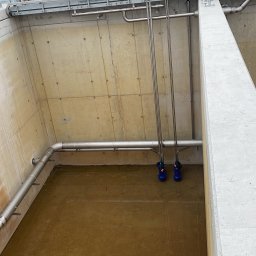 Paweł Kowalski P.K.-SPAW - Betonowy zbiornik z rurami i stojącą wodą, widok z góry, fragment konstrukcji stalowej w tle.