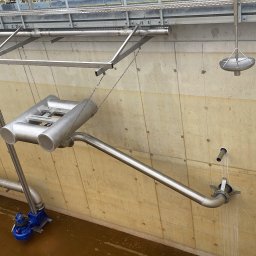 Paweł Kowalski P.K.-SPAW - Instalacja przemysłowa z rurami i pompą w betonowym zbiorniku, widoczne elementy konstrukcji stalowej podwieszone na łańcuchach, ściekająca woda.