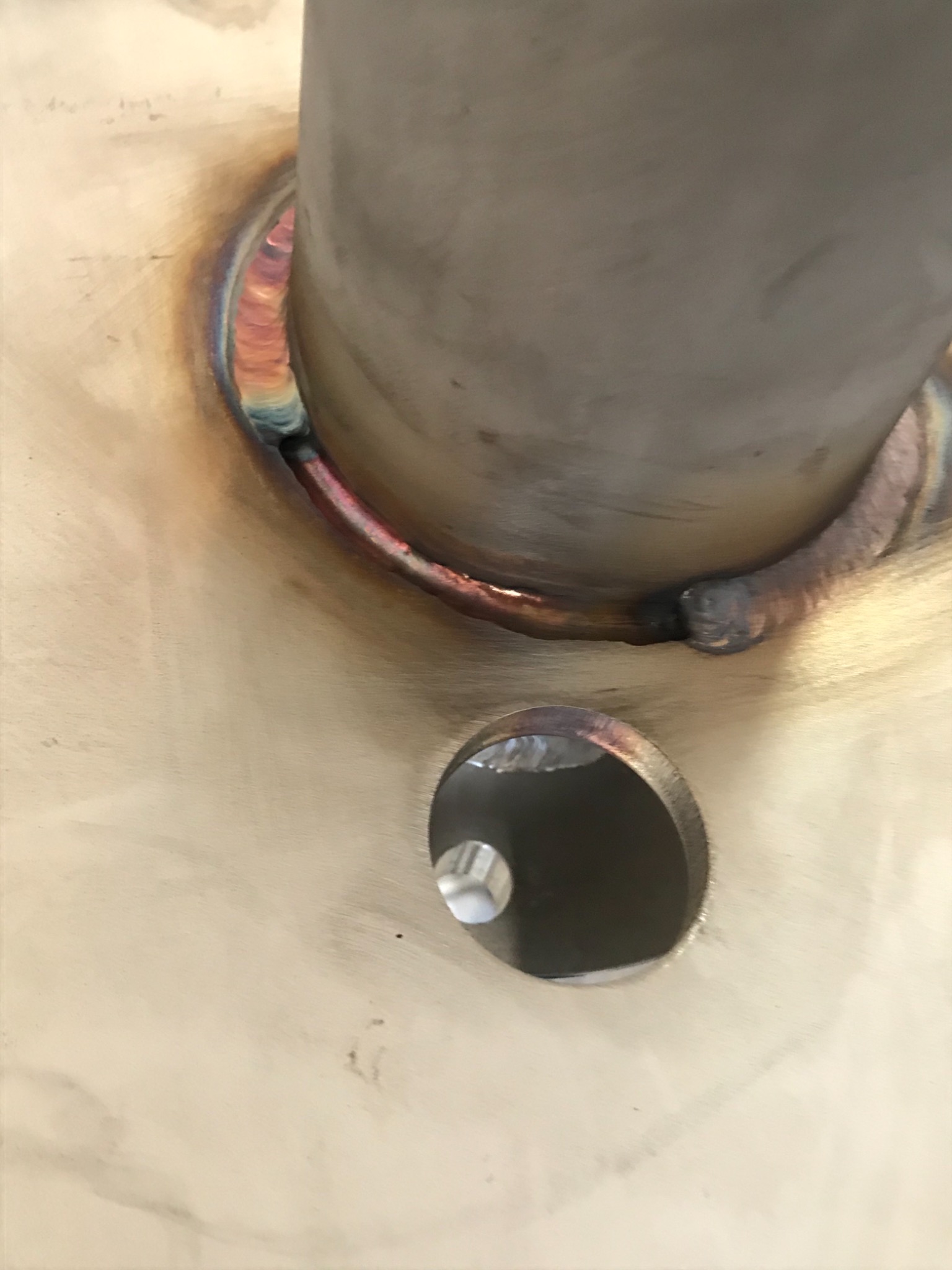 Wspawana rura w metalową płytę, widoczne ślady spawania z charakterystycznymi przebarwieniami termicznymi i otwór w płycie z wykończeniem krawędzi.