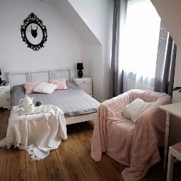 Direct Sales Center - Jasna sypialnia na poddaszu z łóżkiem, stolikami nocnymi, fotelem obitym różowym pluszem i dekoracyjnym czarnym ornamentem na ścianie.