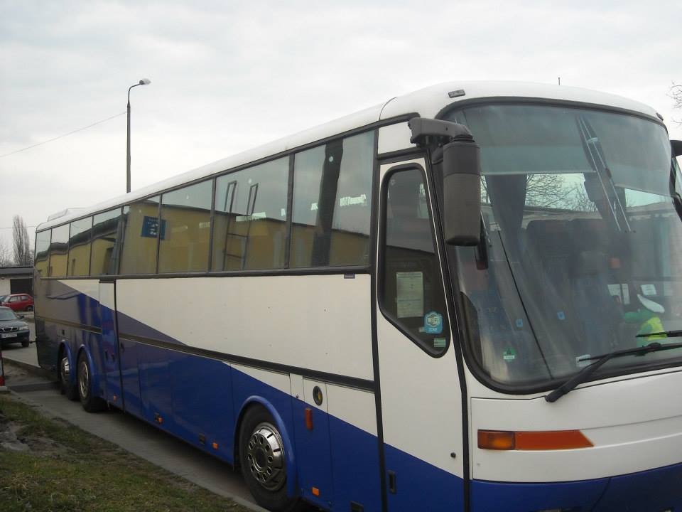 Autokar Bova w barwach biało-niebieskich, widok z boku, zaparkowany na zewnątrz, z widocznymi odbiciami budynków w oknach.