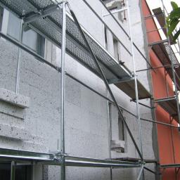 Protech - Budynek w Strzelinie w trakcie ocieplania, widoczne rusztowania i warstwa izolacyjna z szarego styropianu z czarnymi plamkami. Fragment ściany pomalowany na pomarańczowo.