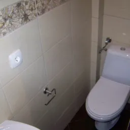 Jasna łazienka z dekoracyjnymi płytkami z motywem kwiatowym, widoczny fragment umywalki, toaleta, uchwyt na papier toaletowy i gniazdko elektryczne.