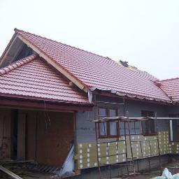 Protech - Dom jednorodzinny w trakcie budowy, z częściowo ocieploną elewacją i nowym, czerwonym dachem z dachówki ceramicznej, widoczne rusztowania i materiały budowlane.