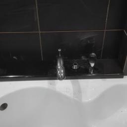 Protech - Biała umywalka z chromowaną baterią i czarną, błyszczącą płytką ceramiczną na ścianie, widoczne ślady po montażu.