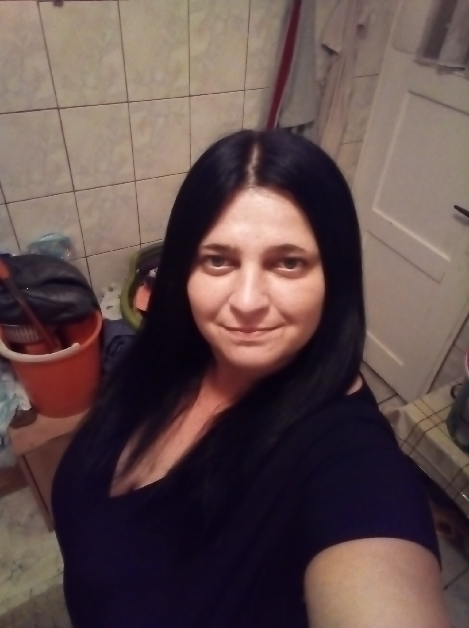 Autoportret kobiety z długimi, czarnymi włosami, na tle łazienki z wiadrem i mopem