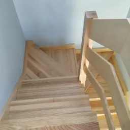 Nowoczesne drewniane schody z jasnego drewna, widok od dołu, minimalistyczny design z ukośnymi wzorami na boku.