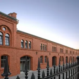 Odrestaurowany, ceglany budynek z czarną, metalową balustradą, widok z zewnątrz, tabliczka z nazwą ulicy 'Wyspiańskiego 29'.