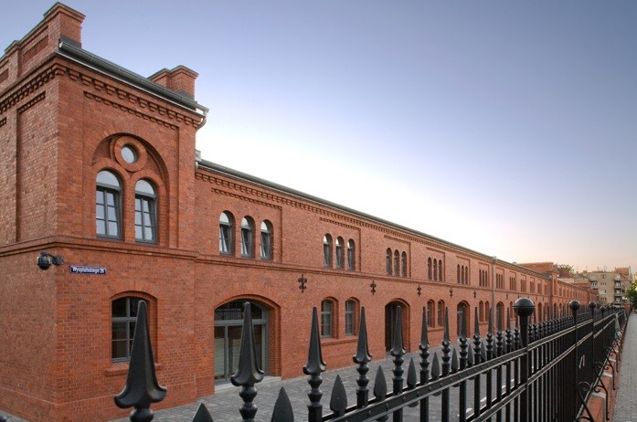 Odrestaurowany, ceglany budynek z czarną, metalową balustradą, widok z zewnątrz, tabliczka z nazwą ulicy 'Wyspiańskiego 29'.