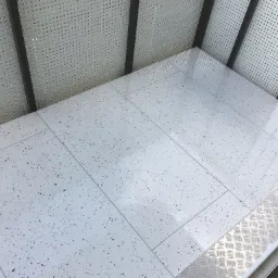 Białe płytki podłogowe w stylu lastryko na balkonie z perforowaną balustradą, widoczny fragment metalowego progu.