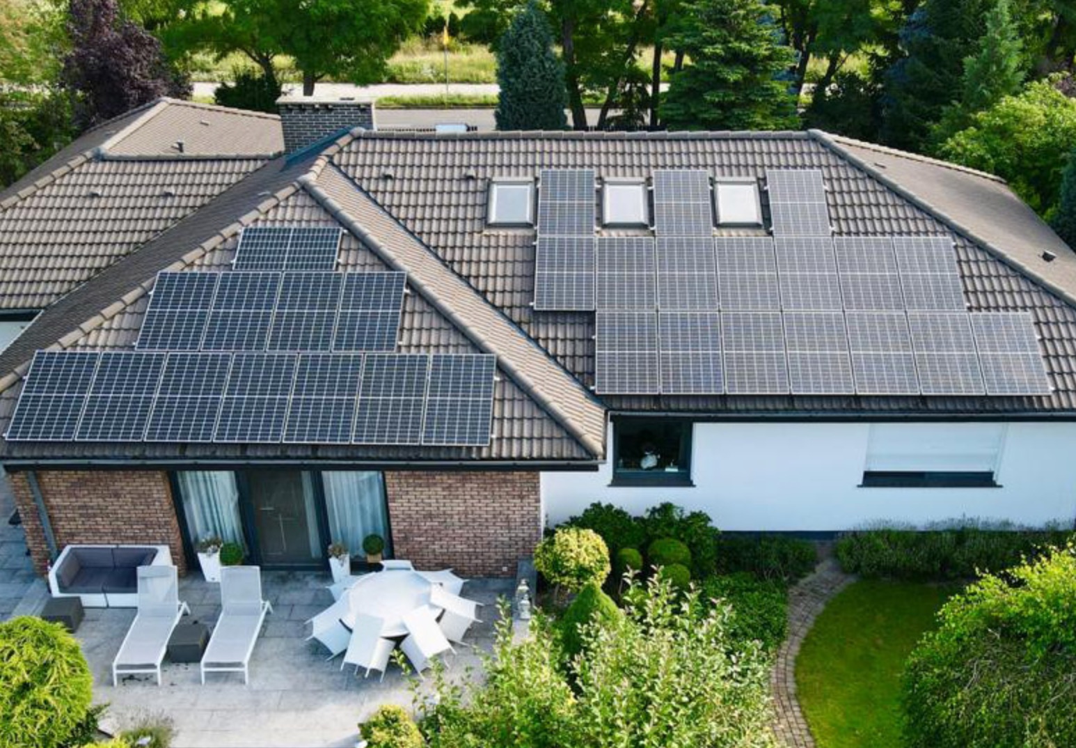 Dom z panelami słonecznymi na dachu, widok z góry, z elementami ceglanymi i białymi ścianami, patio z białymi meblami ogrodowymi.