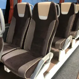 Wnętrze autobusu turystycznego z brązowo-beżowymi siedzeniami z regulowanymi zagłówkami i gniazdkami elektrycznymi pod siedzeniami.