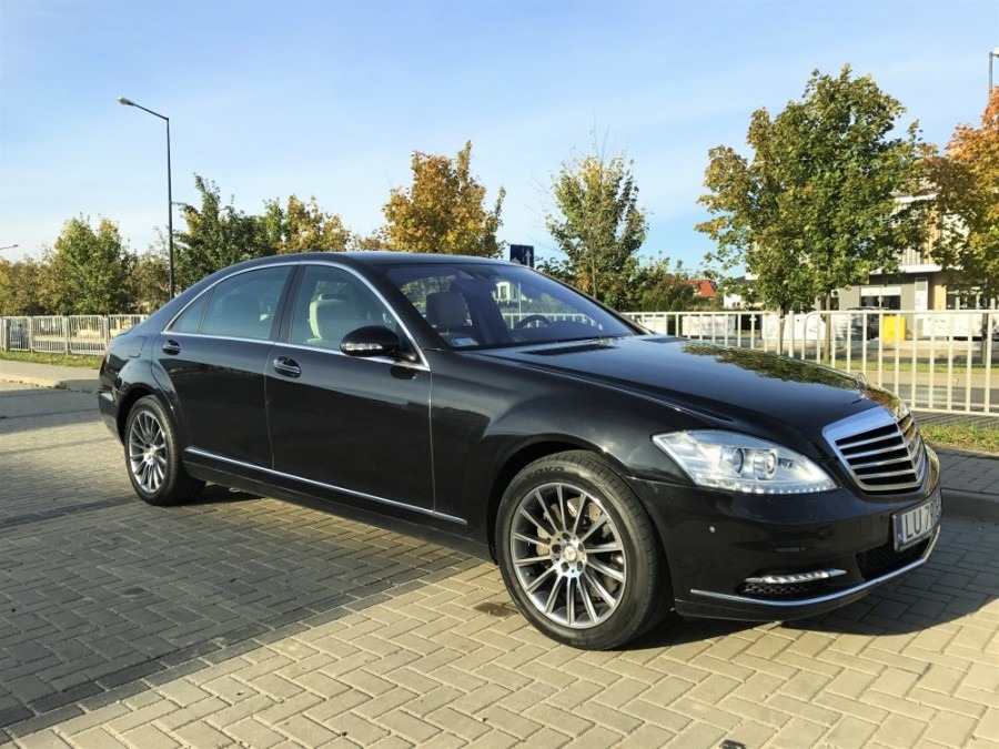 Czarna limuzyna Mercedes-Benz S-Class na brukowanym parkingu w słoneczny dzień, widoczne srebrne felgi i chromowane detale.