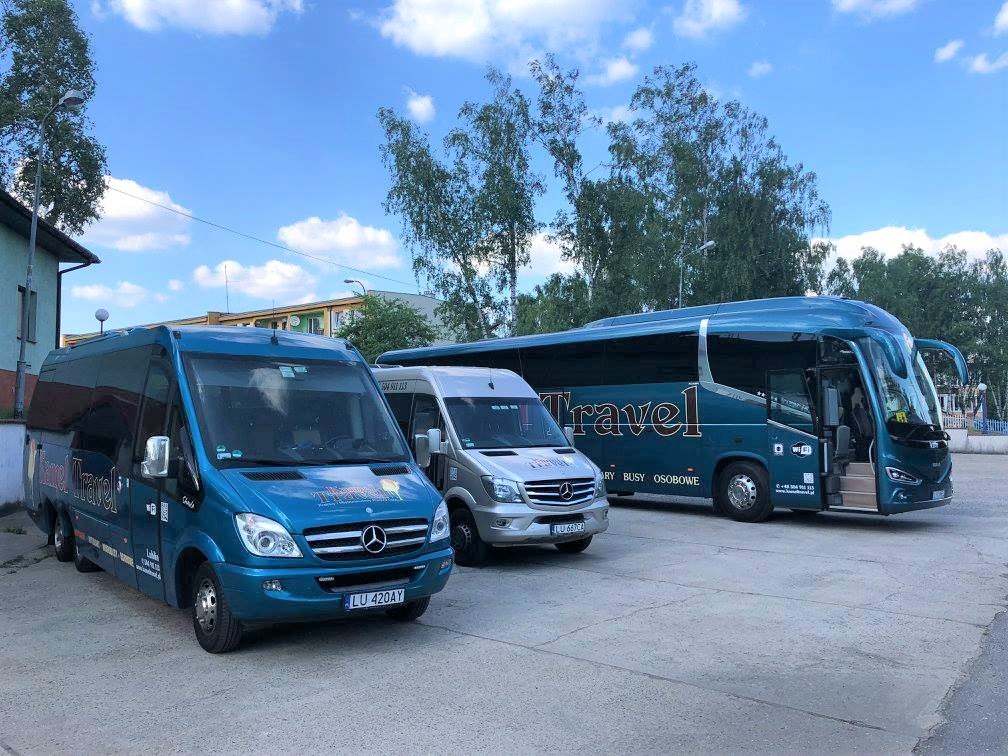 Flota firmowa: Niebieski bus z logo Time Travel i numerem rejestracyjnym LU 420AY, srebrny bus oraz turkusowy autokar na betonowym placu pod błękitnym niebem z białymi chmurami.