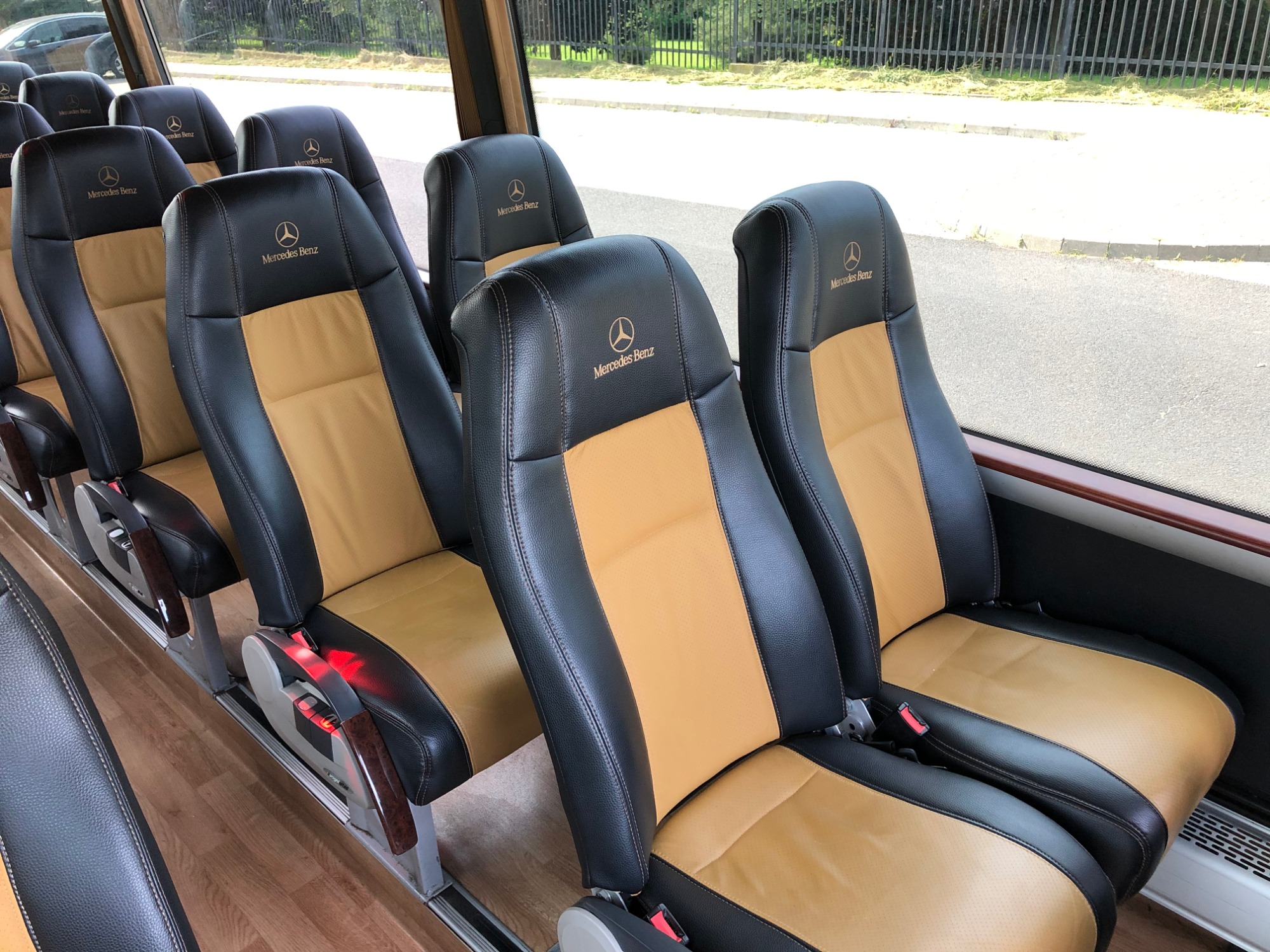 Wnętrze autobusu z rzędami czarno-beżowych skórzanych foteli z logo Mercedes-Benz na zagłówkach, widok z perspektywy pasażera.