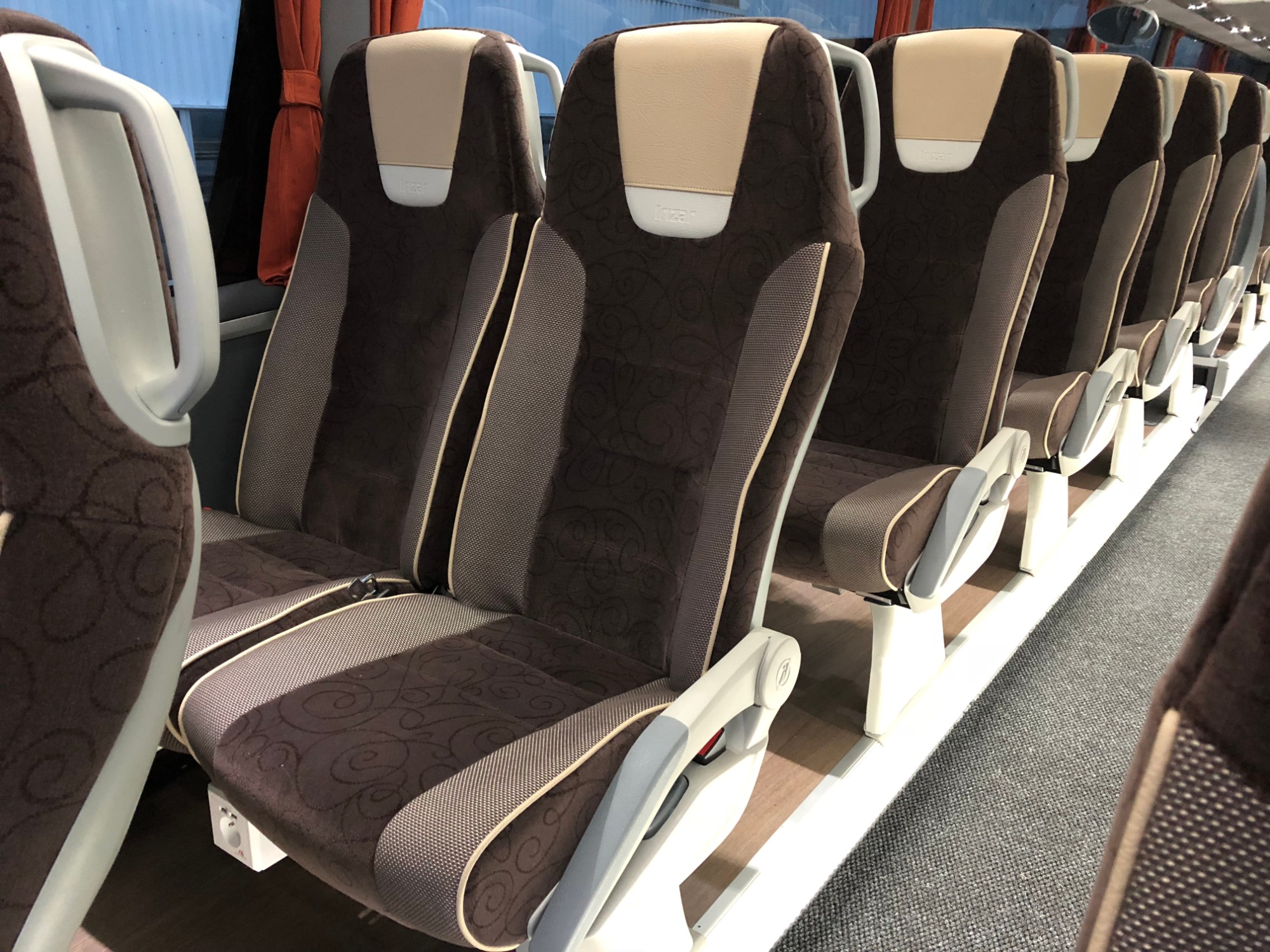 Wnętrze autobusu turystycznego z brązowo-beżowymi siedzeniami z regulowanymi zagłówkami i gniazdkami elektrycznymi pod siedzeniami.