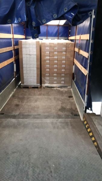 Wnętrze naczepy z załadowanymi paletami kartonów, zabezpieczonych folią stretch, widok od strony rampy załadunkowej.