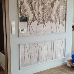 Oskar Hadrian - Ściana w Chwałowicach z dekoracyjnymi panelami z motywem liści i abstrakcyjnymi pionowymi liniami, oświetlona złotym kinkietem, z drewnopodobną podłogą ułożoną w jodełkę.