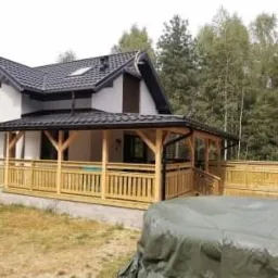 Nowoczesny dom z drewnianą konstrukcją tarasu i balustradami, widok na las w tle.