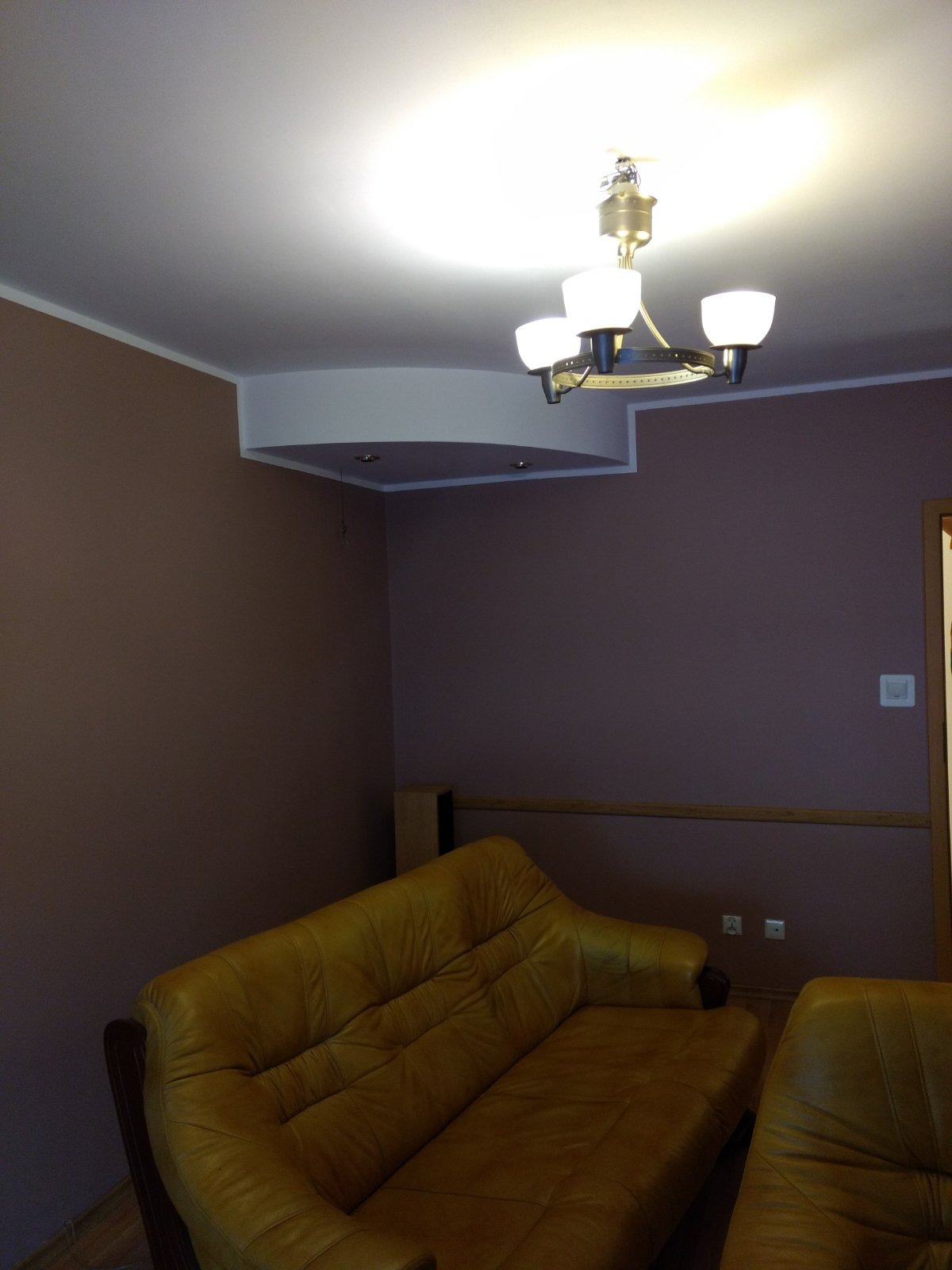 Pokój z brązowymi ścianami, żółtą skórzaną kanapą i białym sufitem podwieszanym z oświetleniem punktowym oraz wiszącą lampą.