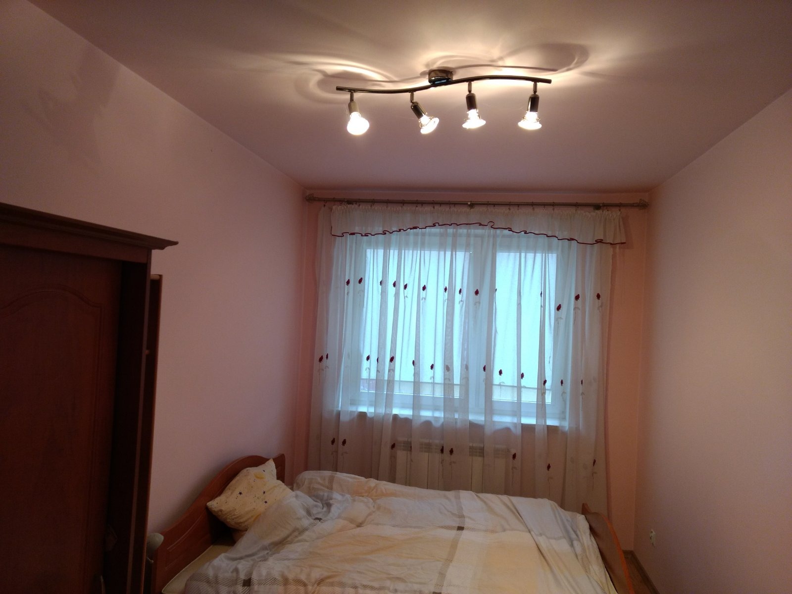 Różowy pokój z łóżkiem, szafą i lampą sufitową z czterema reflektorami