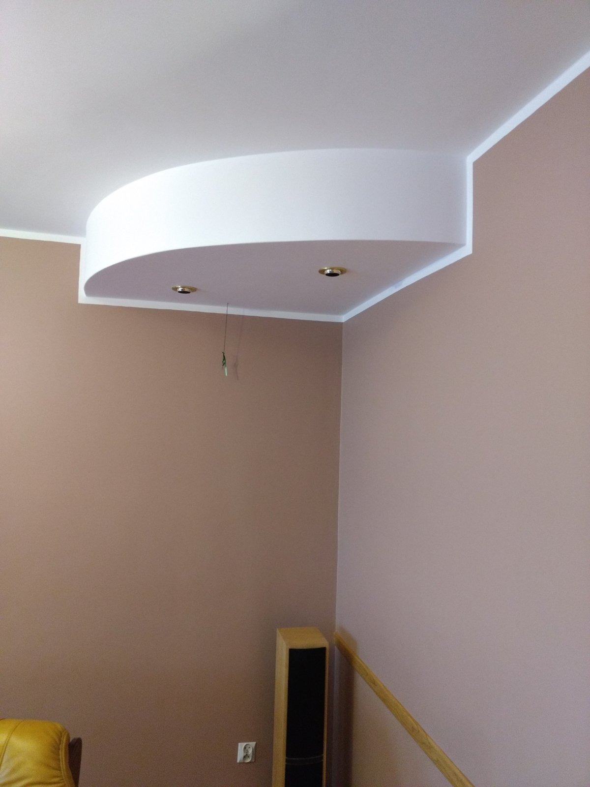 Kremowo-brązowe ściany w rogu pokoju z dwoma wbudowanymi punktami świetlnymi w ozdobnej, półokrągłej strukturze sufitowej z białym obramowaniem.