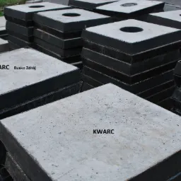Stosy kwadratowych, prefabrykowanych płyt z otworami, ułożone na palecie, z widocznym napisem 'KWARC Busko Zdrój' na jednej z płyt.