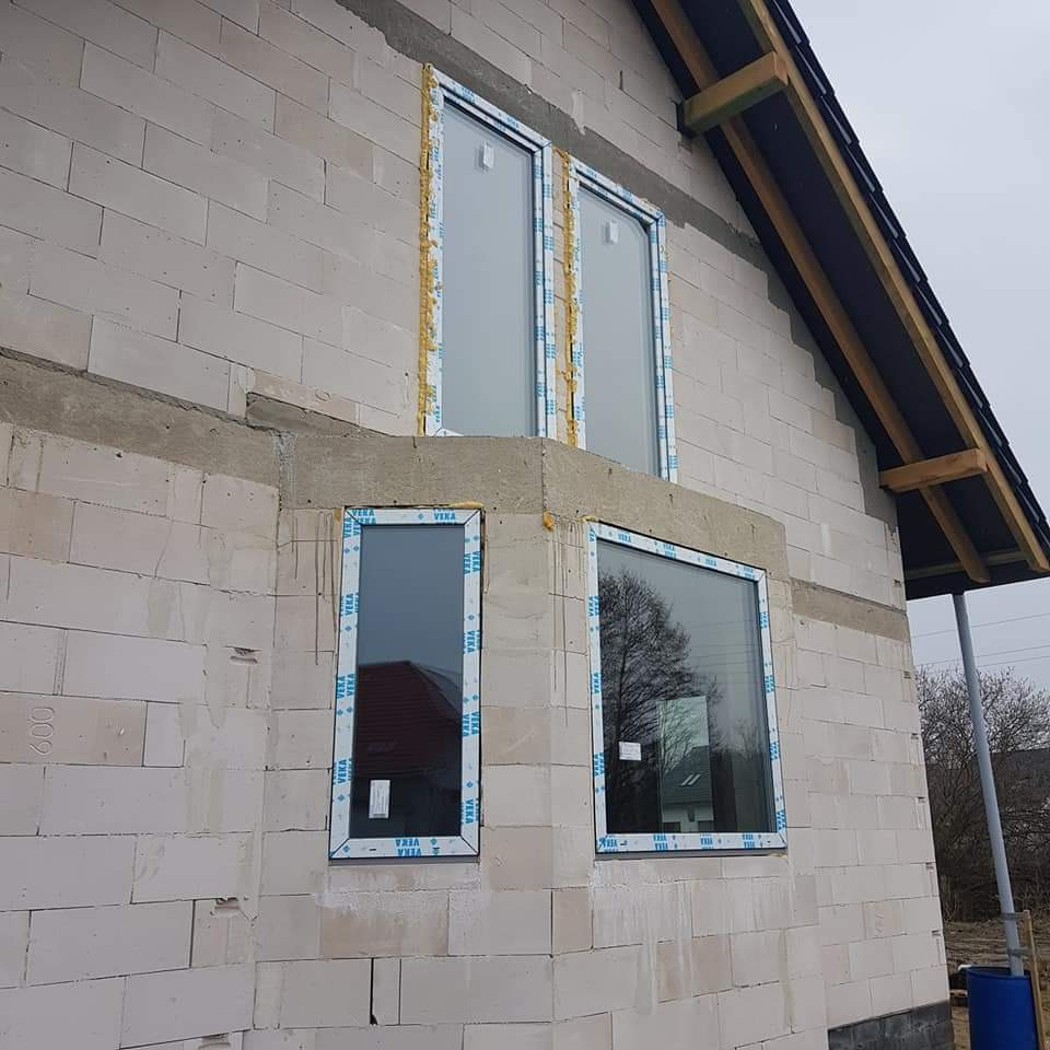 Nowo zamontowane okna PCV marki VEKA w surowym domu z betonu komórkowego, widoczne ślady pianki montażowej, dach w trakcie budowy.