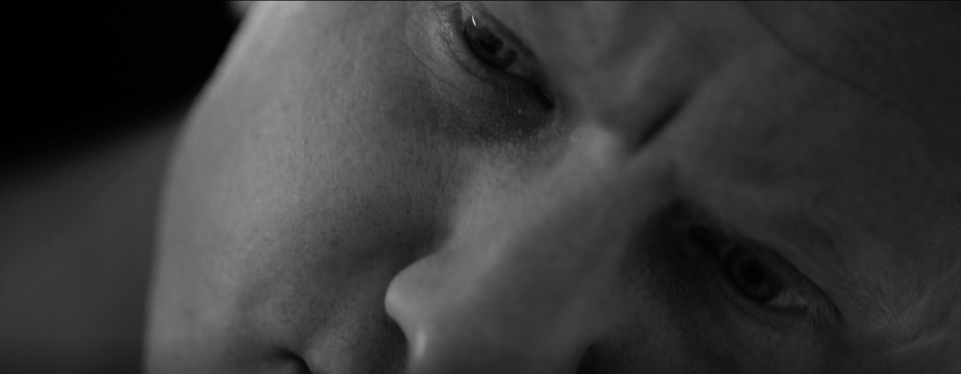 Czarno-białe, zbliżone ujęcie twarzy osoby z widocznymi detalami skóry i oczu, ustawione pod kątem.