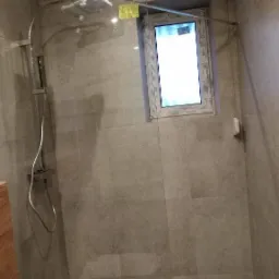 Nowoczesna kabina prysznicowa z szarą płytką, przeszkloną ścianką i oknem z widokiem na zewnątrz, z odpływem liniowym w podłodze.