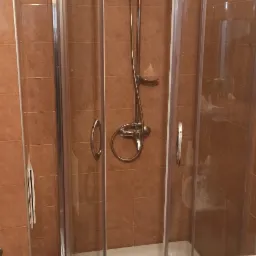 Kabina prysznicowa z deszczownicą i baterią termostatyczną w łazience z brązowymi płytkami.