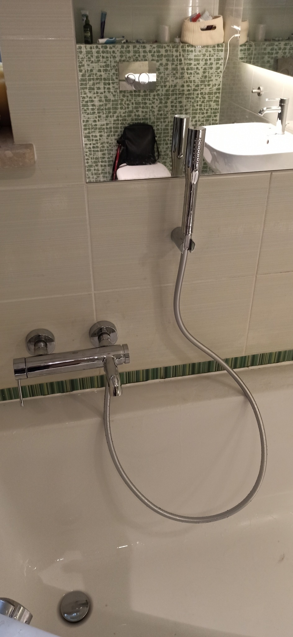 Bateria wannowa z prysznicem zamontowana na ścianie wyłożonej jasnymi płytkami, widoczny odpływ w wannie.